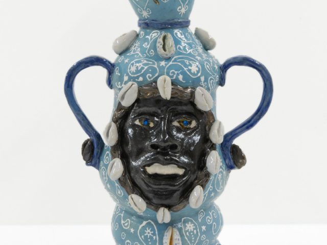 A ceramic vessel with a blue glaze and a dark face in the center.