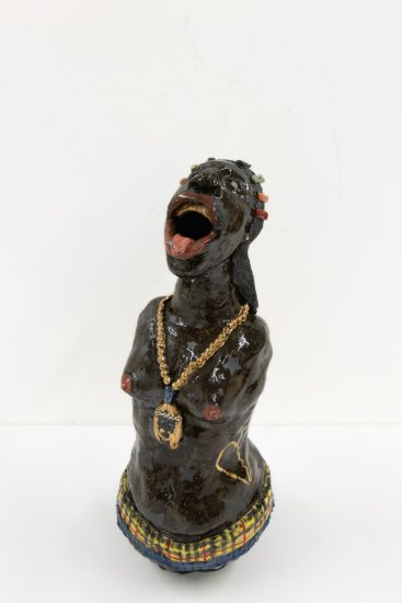 A ceramic vessel with dark brown glazing depicting a figure with no shirt and a gold chain.