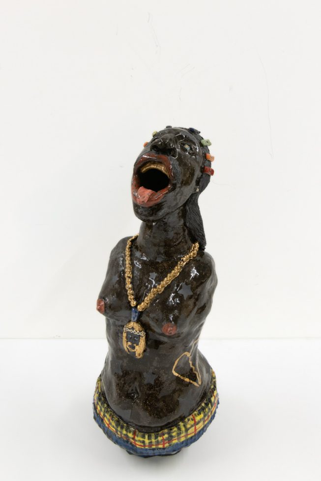 A ceramic vessel with dark brown glazing depicting a figure with no shirt and a gold chain.
