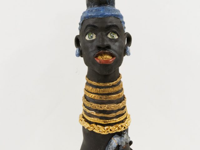 A ceramic vessel depicting a figure with gold necklaces, rings, and a watch.