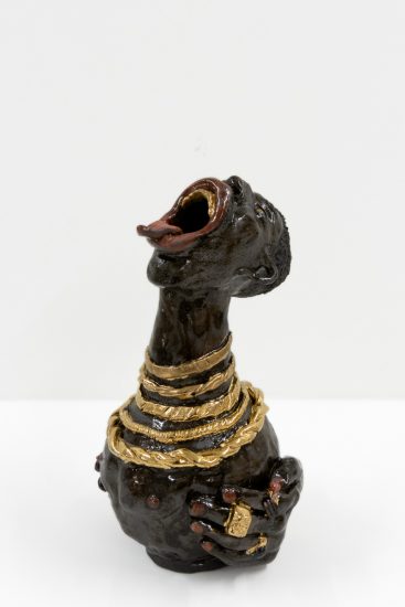 A ceramic vessel with dark brown glazing of a figure with an open mouth and gold necklaces.