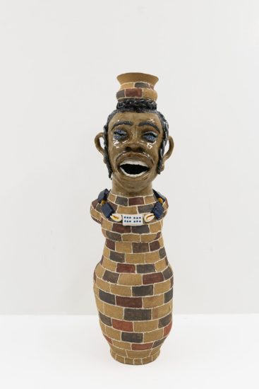 A glazed ceramic vessel depicting a tall figure with a brink body.