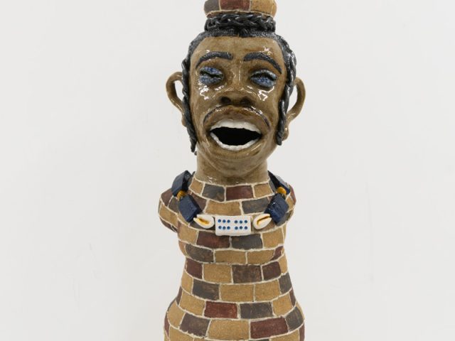 A glazed ceramic vessel depicting a tall figure with a brink body.