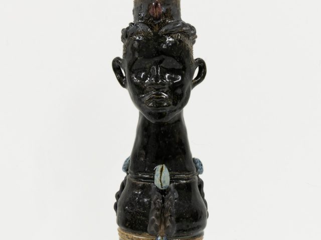 A ceramic vessel with a dark brown glaze adorned with shells depicting a tall human figure.