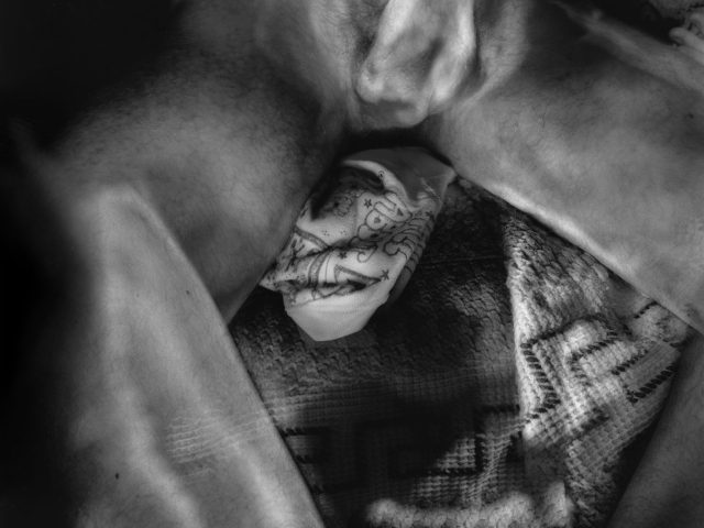 This black and white photograph shows a naked man sprawled across a blanket in an apartment.