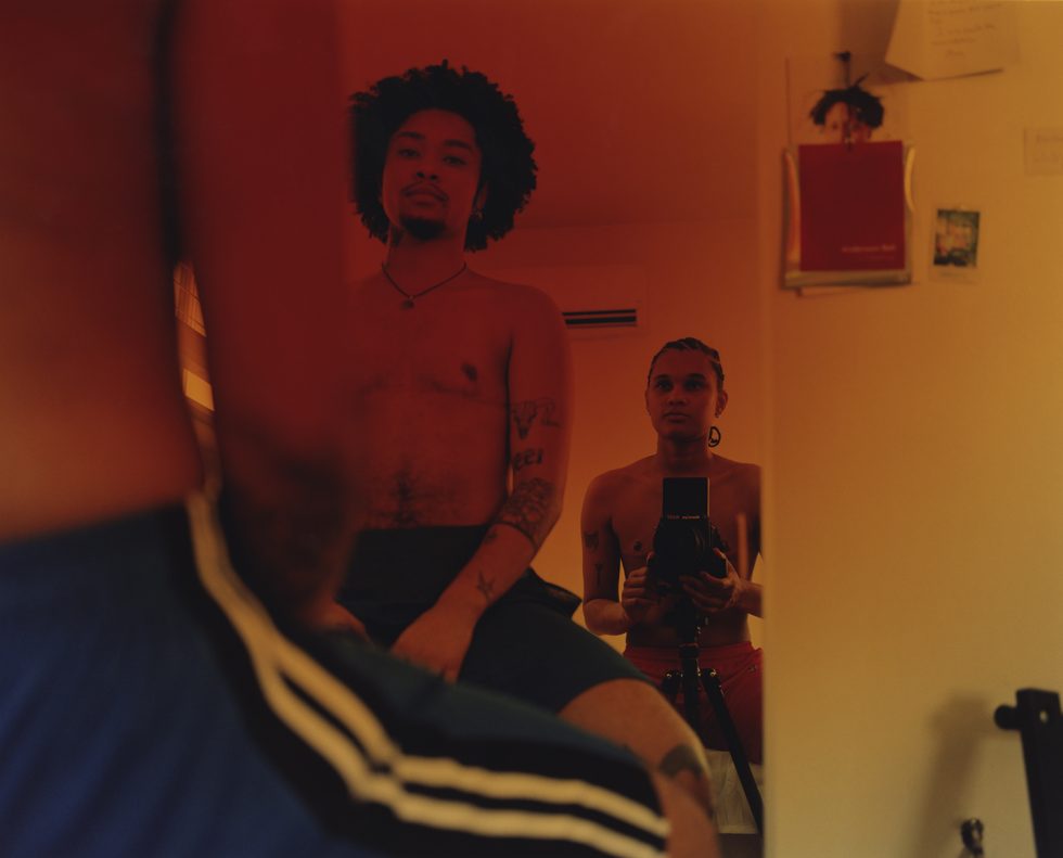In this color photograph, the photographer and another person sit in front of a mirror. The image is mostly composed of the reflection, where we see them staring into the glass.