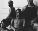 In this black and white photograph, four sitting figures lean against one another and stare at the camera.