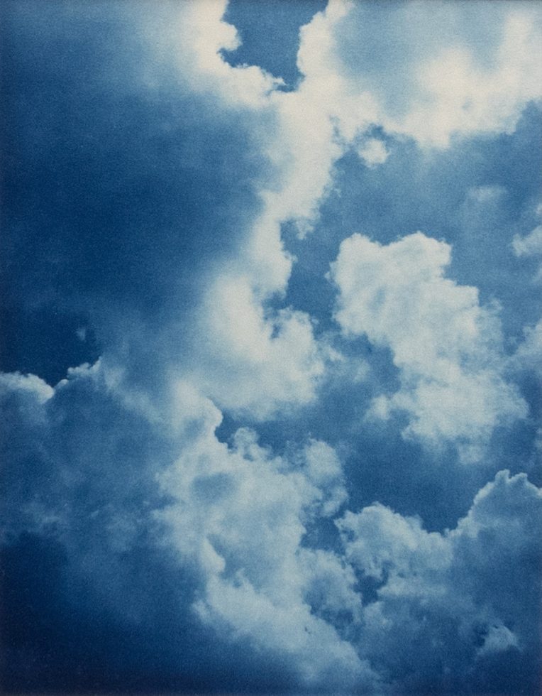 This color photograph shows the sky filled with puffy white clouds.