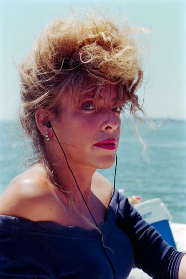 This color photograph is a portrait of a woman from the chest up. She has red hair piled on her head and wears ear buds.