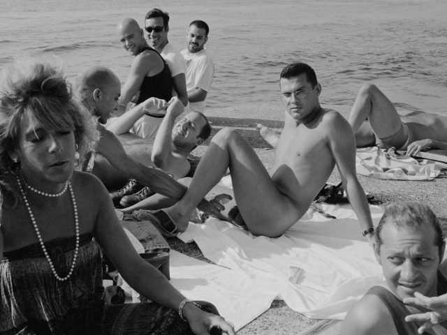 This black and white photograph shows a crowd of people sitting on the pier, looking at the camera.