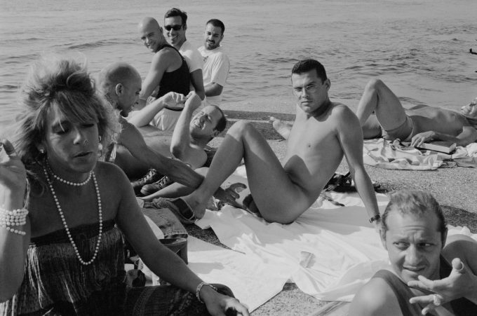 This black and white photograph shows a crowd of people sitting on the pier, looking at the camera.