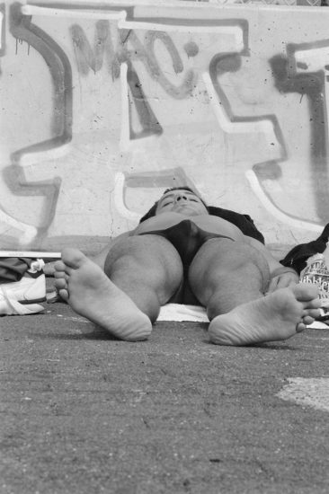 This vertical black and white photograph shows a man lying flat on his back on concrete.