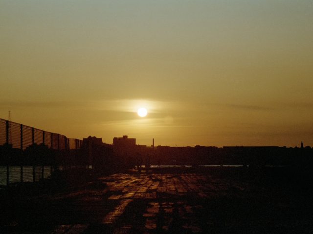 This color photograph shows a yellow sunset, setting above the skyline of New York City.