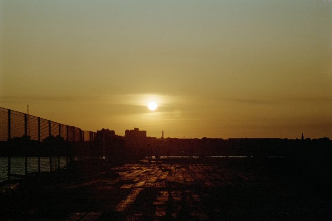This color photograph shows a yellow sunset, setting above the skyline of New York City.