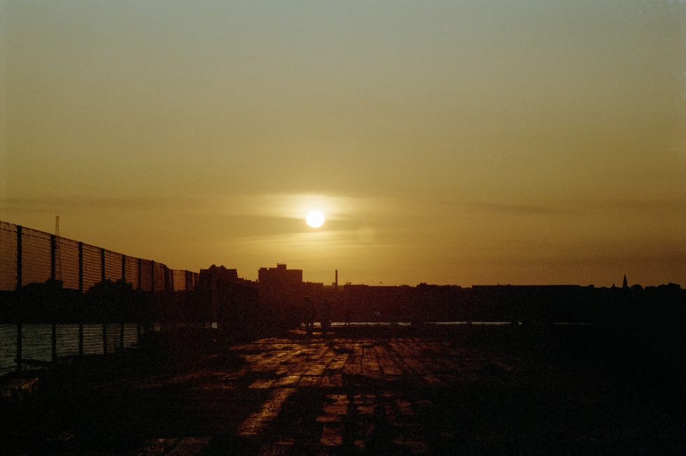This color photograph shows a yellow sunset, setting above the skyline of New York City.