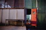 This color photograph shows the facade of an industrial building with an orange door.