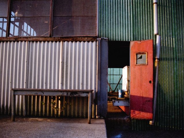 This color photograph shows the facade of an industrial building with an orange door.