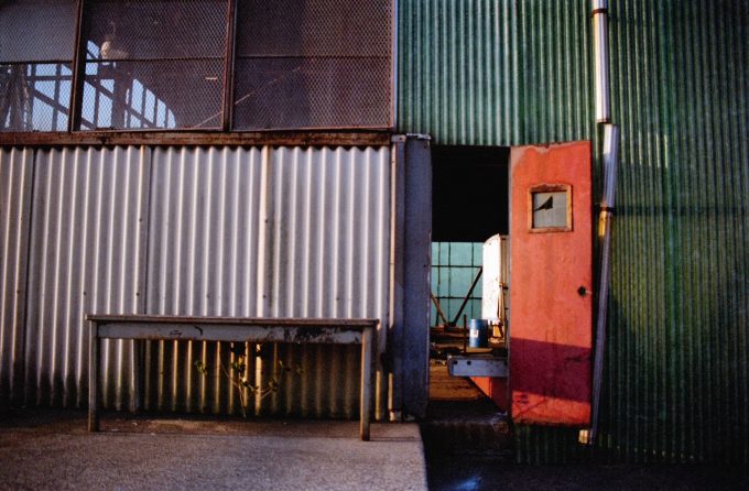 This color photograph shows the facade of an industrial building with an orange door.
