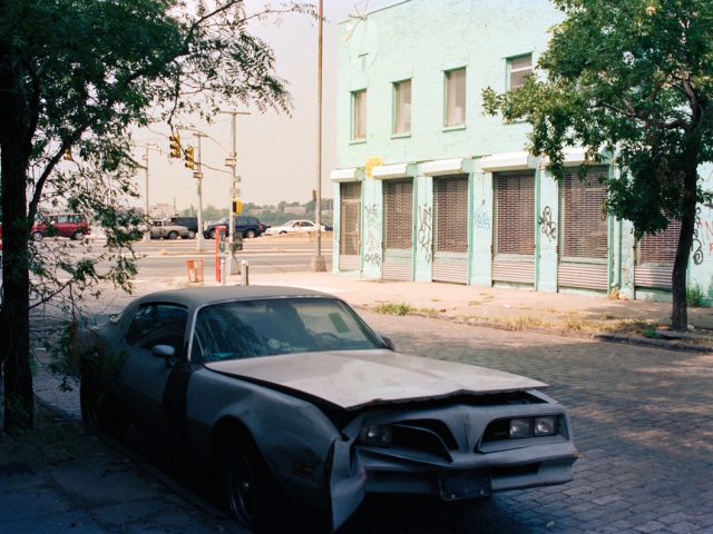 This color photograph shows a blue car parked on the street outside a bright blue building.