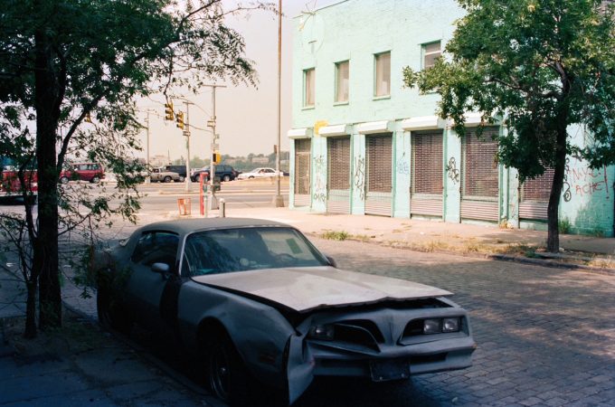 This color photograph shows a blue car parked on the street outside a bright blue building.