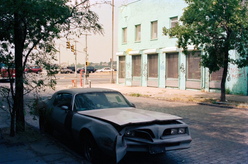 This color photograph shows a blue car parked on the street outside a bright blue building.