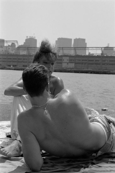 This black and white photograph shows the back of a shirtless man overlooking the New York skyline on a pier.