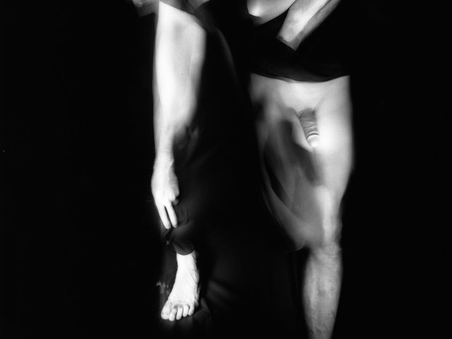 This black and white photograph shows multiple human limbs, glowing white against a black background.