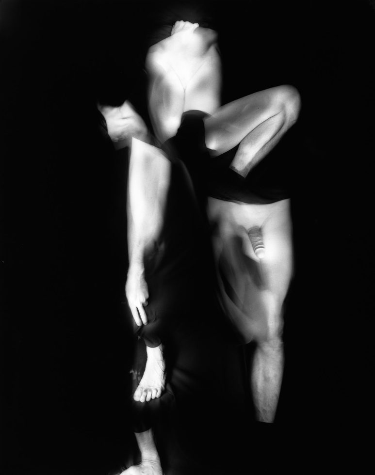 This black and white photograph shows multiple human limbs, glowing white against a black background.
