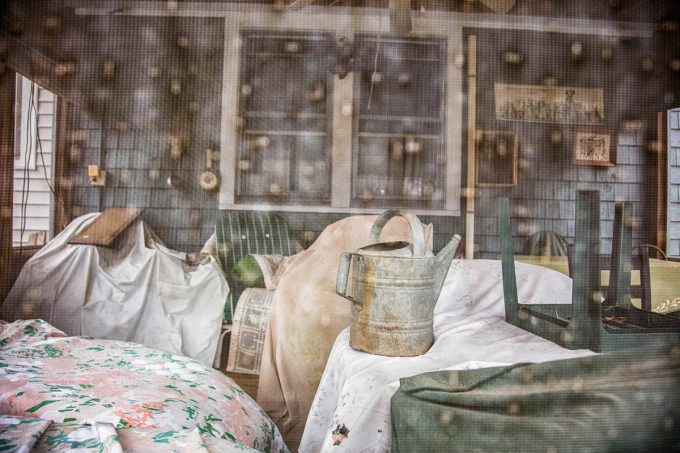This color photograph shows a screened in porch with some chairs and a watering can.
