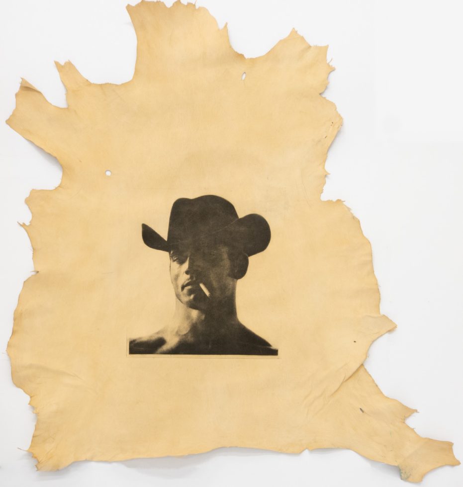 This is a photograph of a man in a cowboy hat, seen from the neck up, printed on an animal hide.