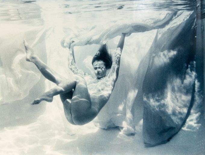 This photograph shows a naked woman floating underwater against a background of billowing fabric.