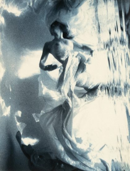 This photograph shows a woman floating underwater surrounding by billowing fabric.