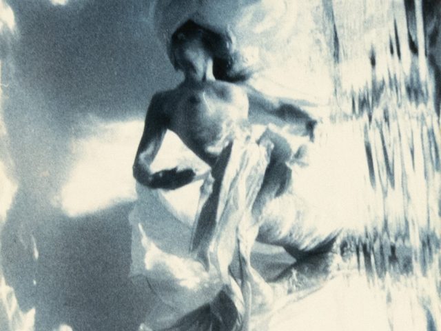 This photograph shows a woman floating underwater surrounding by billowing fabric.