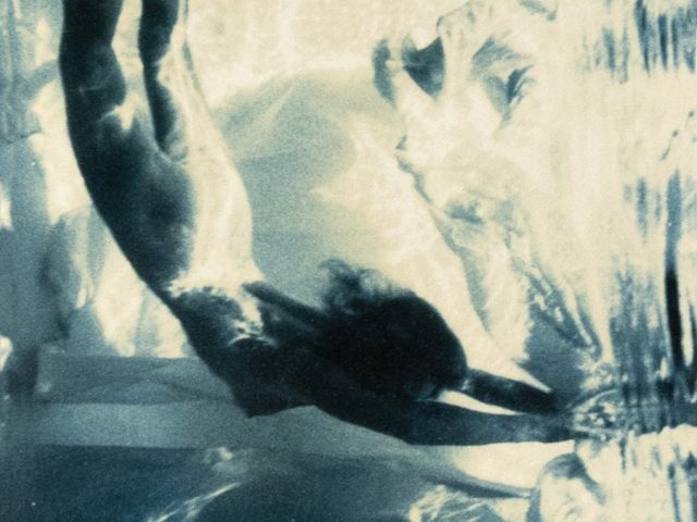 This photograph shows a naked woman diving underwater with a fantastical background of silk.