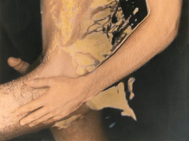 This photograph shows a naked man lying on his side in dark water.