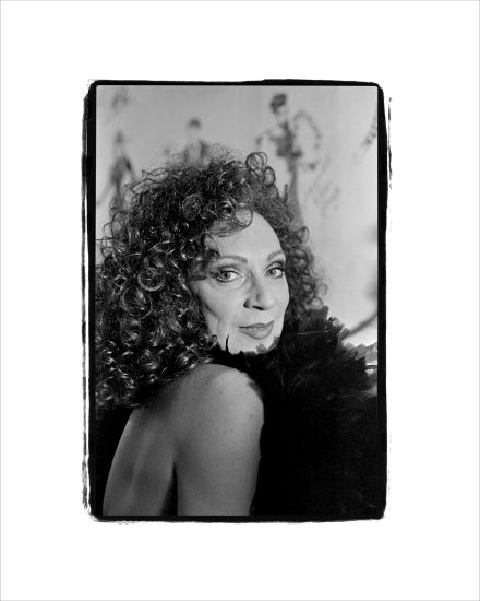 This black and white photograph shows a person with curly hair wearing a black feathered boa.