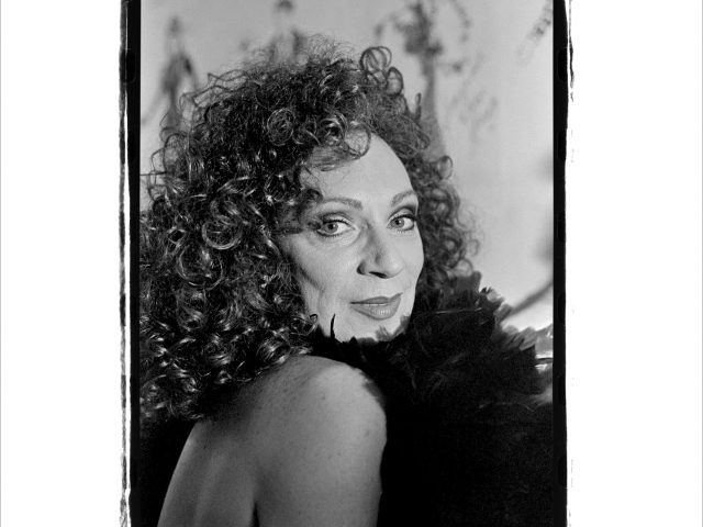 This black and white photograph shows a person with curly hair wearing a black feathered boa.
