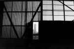 This black and white photographs shows a building seen through an opening in the dark facade of another building under construction.