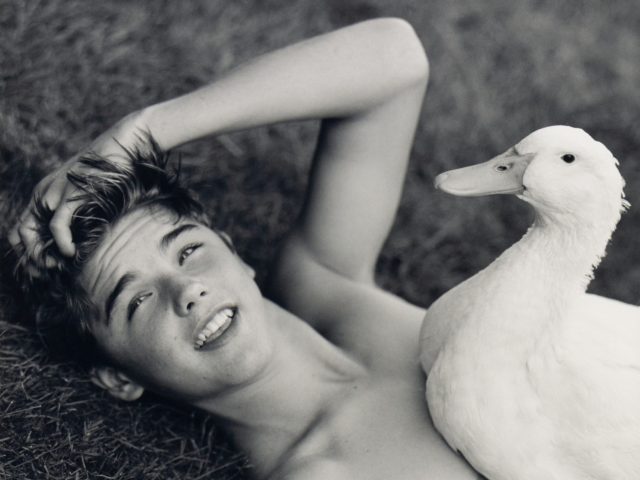 This is a black and white photograph of a shirtless man and a duck.