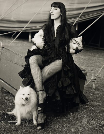 This is a black & white photograph of a woman with three small white dogs.