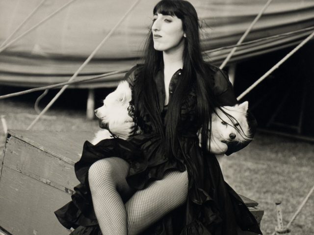 This is a black & white photograph of a woman with three small white dogs.