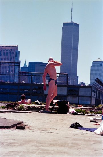 This color photograph shows a man posing in front of a Manhattan skyline.