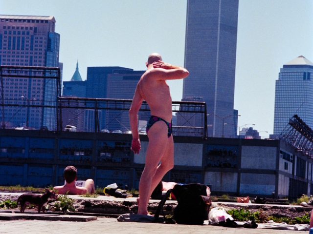 This color photograph shows a man posing in front of a Manhattan skyline.