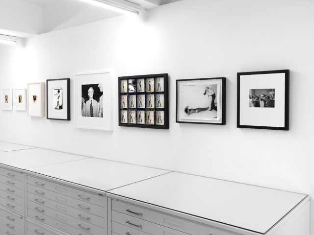 This photograph shows the walls of a gallery where framed photographs hang in a line.