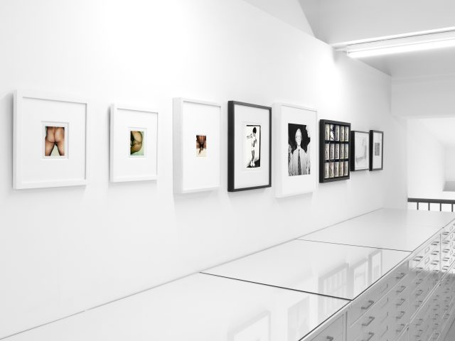This photograph shows a series of photographs on the white walls of a gallery.