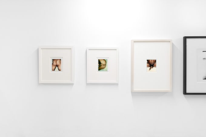 This photograph shows the walls of a gallery where photographs depicting naked body parts hang.