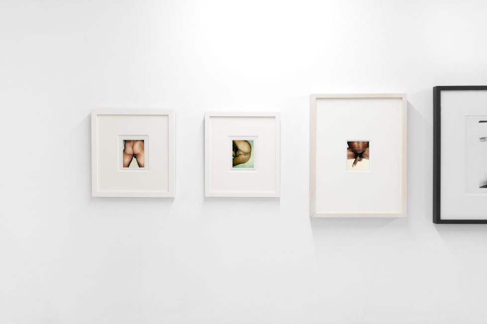 This photograph shows the walls of a gallery where photographs depicting naked body parts hang.
