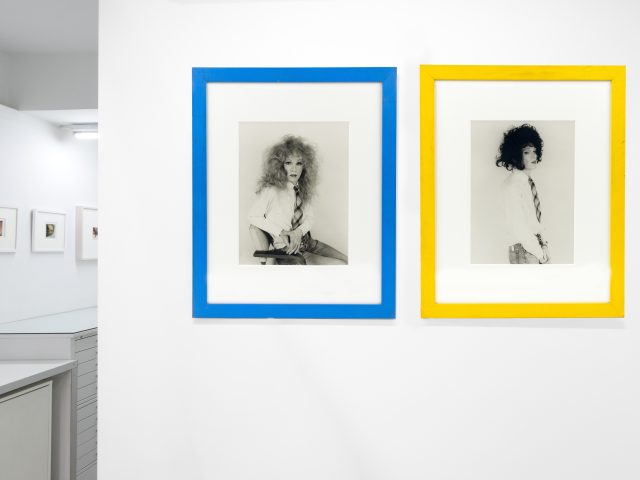 This photograph shows black and white photographs of men in wigs framed in bright colors.