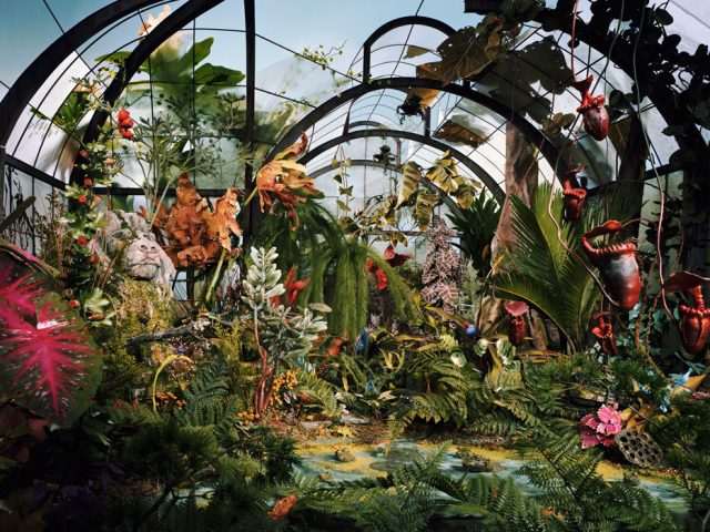 A color photo of an overgrown and forgotten botanical garden constructed from paper, clay, and other materials.