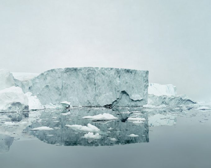 A grayish-blue photo of an iceberg floating with it's reflection below.